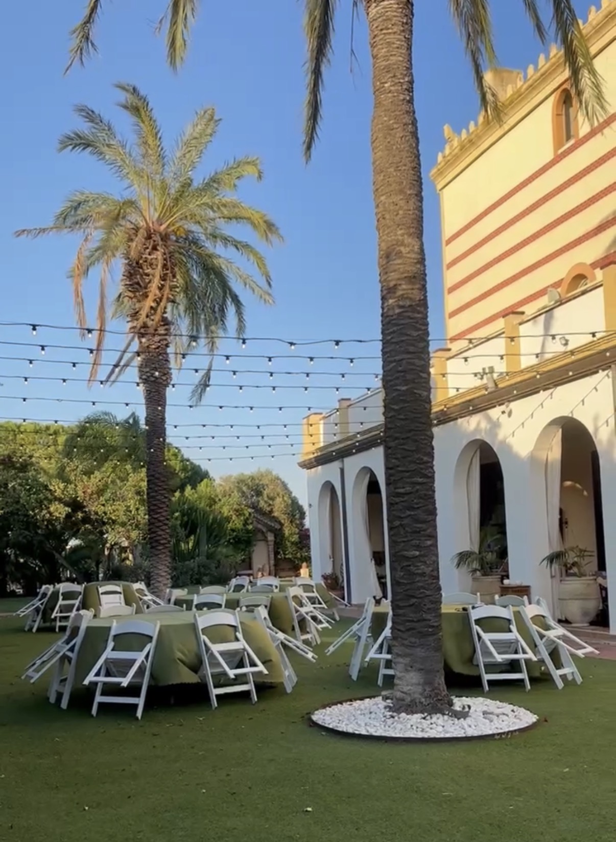 Tables set under the palms with festoon lights strung overhead