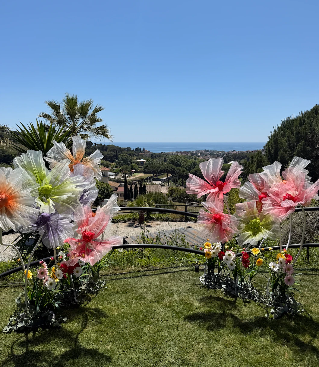 Oversized fabric flowers installed along the lawn, with the sea beyond