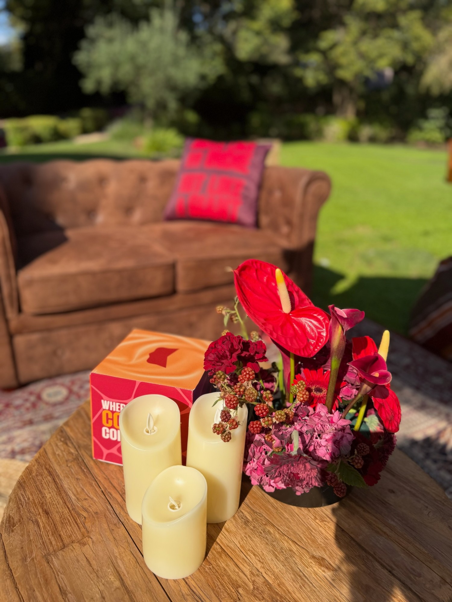 Garden lounge seating with deep red florals and candles on a low wooden table
